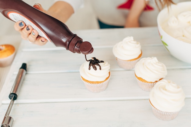 Een jong meisje versiert cupcakes door chocoladeroom te gieten