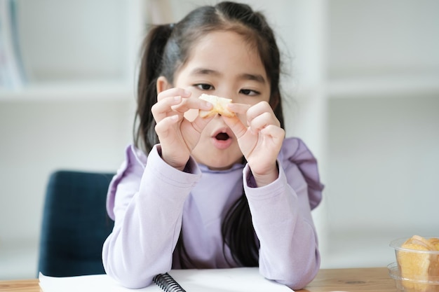 Een jong meisje zit aan een tafel met een stuk eten in haar hand.