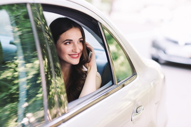 Een jong meisje zit op de achterbank van een auto en praat aan de telefoon.