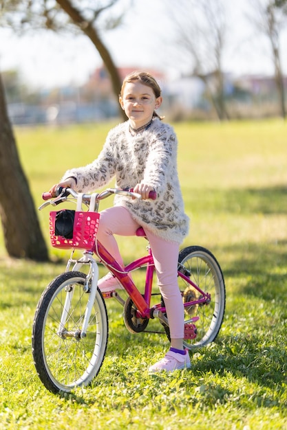 Foto een jong meisje zit op een roze fiets in een park.