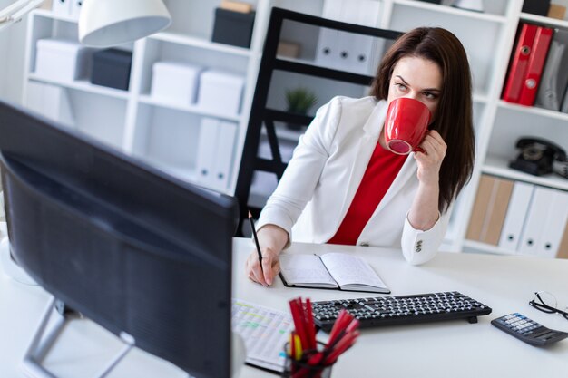 Een jong meisje zit op kantoor op de computer Bureau en houdt een rode kop.