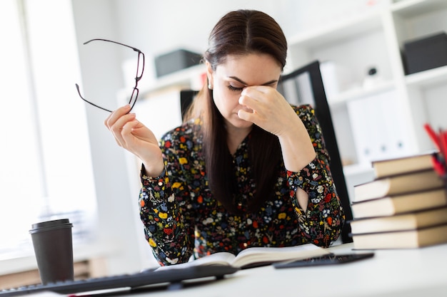 Een jong meisje zit op kantoor op de computer Bureau en werkt met een boek.