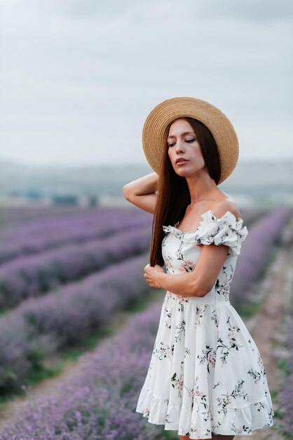 Een jong mooi meisje in een delicate jurk en hoed loopt door een prachtig lavendelveld en geniet van de geur van bloemen Rust en prachtige natuur Lavendel bloeiend en bloemen plukken