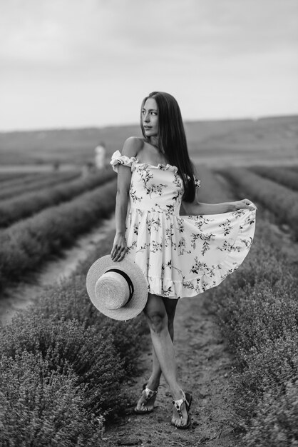 Een jong mooi meisje in een delicate jurk en hoed loopt door een prachtig lavendelveld en geniet van de geur van bloemen. Vakantie en prachtige natuur. Zwart en wit.