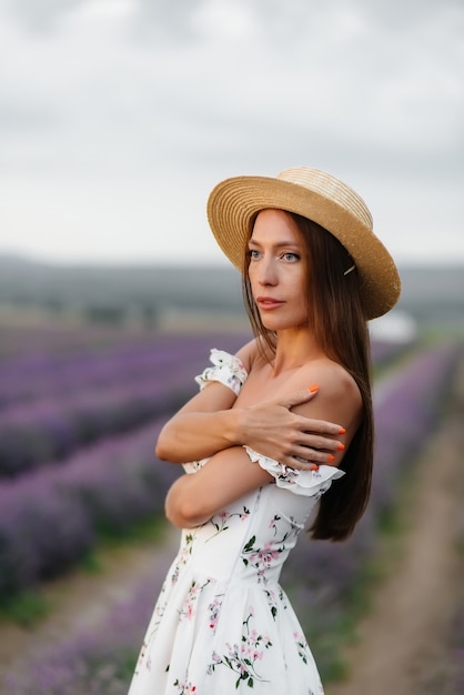 Een jong mooi meisje in een delicate jurk en hoed loopt door een prachtig lavendelveld en geniet van de geur van bloemen. Vakantie en prachtige natuur.