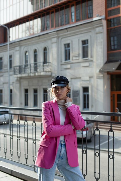 Een jong mooi meisje in een lang roze jasje en een zwarte hoed loopt over straat