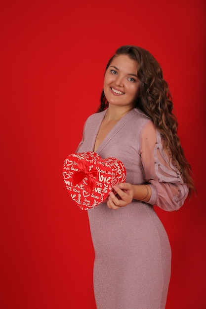 een jong mooi meisje in een roze jurk op de achtergrond houdt een geschenkdoos voor de feestdagen in haar handen