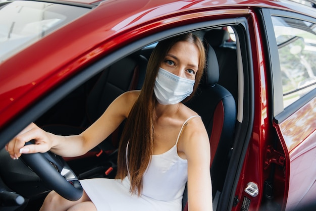 Een jong mooi meisje inspecteert tijdens de pandemie een nieuwe auto bij een autodealer met een masker. De aan- en verkoop van auto's, in de periode van pandemie.