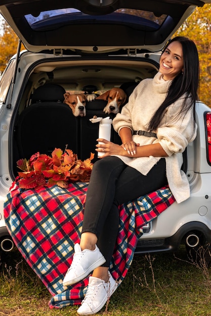 Een jong mooi meisje kwam naar het bos met honden voor een picknick zit in de kofferbak op een gekleurde bla...