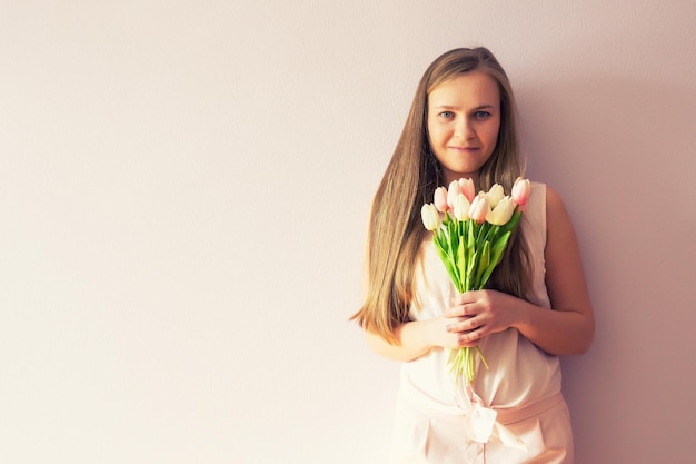 Een jong mooi meisje met blond opgelost lang haar en een vilten hoed op haar hoofd houdt lentebloemen