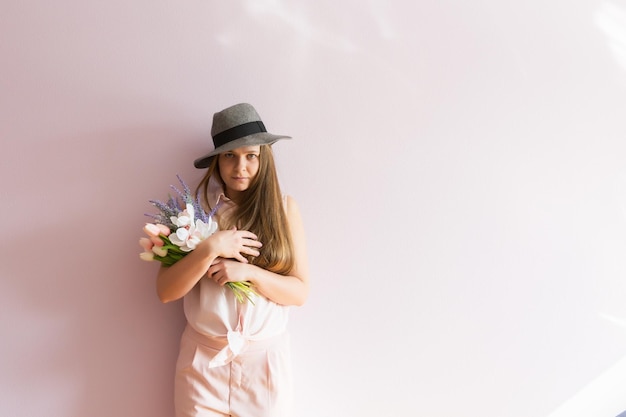 Een jong mooi meisje met blond opgelost lang haar en een vilten hoed op haar hoofd houdt lentebloemen