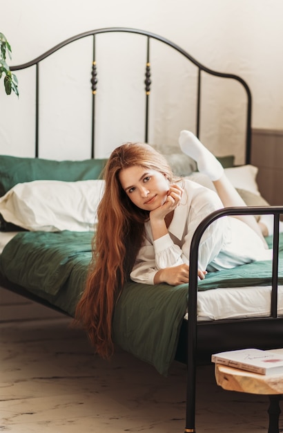 Een jong mooi meisje met lang haar ligt op een bed in de slaapkamer. Dag rust en ontspanning. Verticale foto