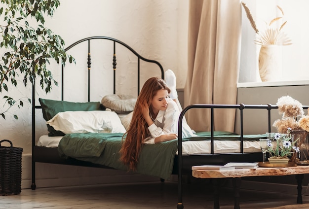 Een jong mooi meisje met lang haar op een bed. Vrouw genieten van ochtend ontwaken. Het concept van huiselijke gezelligheid en comfort.