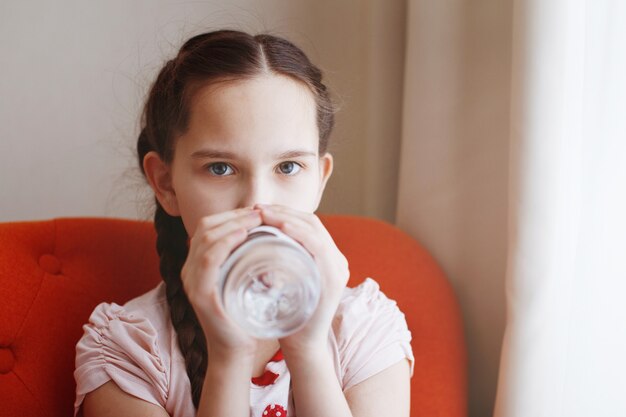 Een jong mooi meisje met vlechten drinkt water uit een fles.