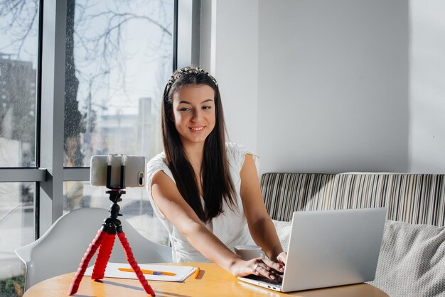 Een jong mooi meisje zit in een café, neemt videoblogs op en chat op sociale netwerken.