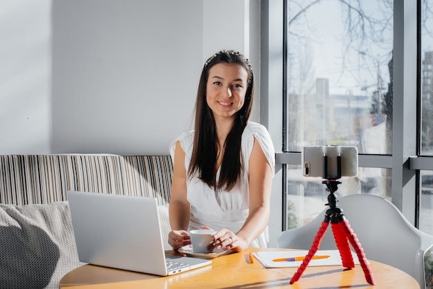 Een jong mooi meisje zit in een café, neemt videoblogs op en chat op sociale netwerken.