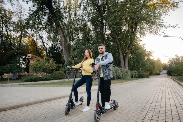 Een jong mooi stel rijdt op elektrische scooters in het park op een warme herfstdag