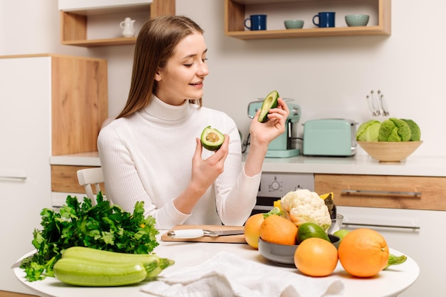 Een jong mooi vegetarisch meisje of blogger bereidt thuis in de keuken een ontbijt van fruit, groenten en groenten blog over gezond eten