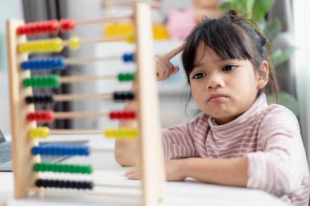Een jong schattig Aziatisch meisje gebruikt het telraam met gekleurde kralen om thuis te leren tellen