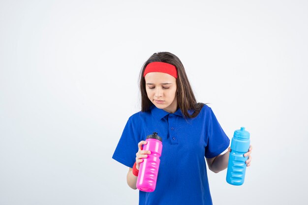 een jong sportief meisje dat kleurrijke flessen water houdt.