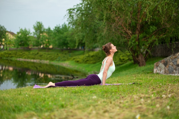 Een jong sportmeisje beoefent yoga op een groen grasveld bij de rivier, yoga verzekert houding.