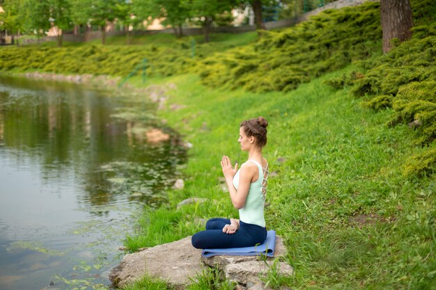 Een jong sportmeisje beoefent yoga op een groen grasveld bij de rivier