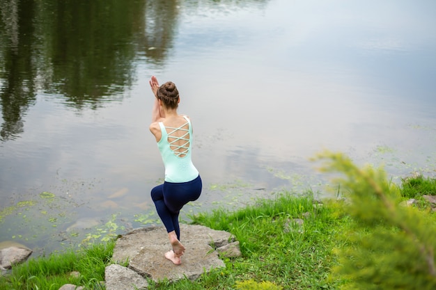 Een jong sportmeisje beoefent yoga op een groen grasveld bij de rivier,