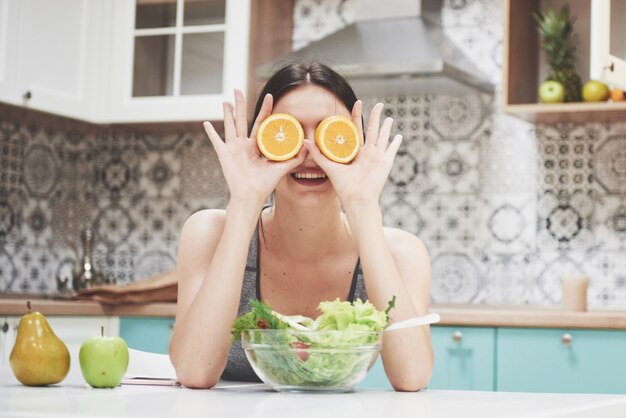 Een jong sportmeisje geniet van een fruitsalade. Speels zijn en haar ogen bedekken met oranje.