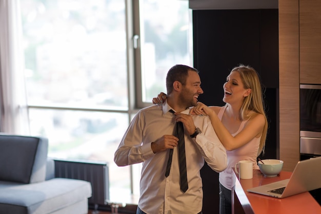 Een jong stel bereidt zich voor op de baan en gebruikt een laptop. De man drinkt koffie terwijl de vrouw samen in een luxe huis ontbijt, glimlachend naar het scherm kijkend.