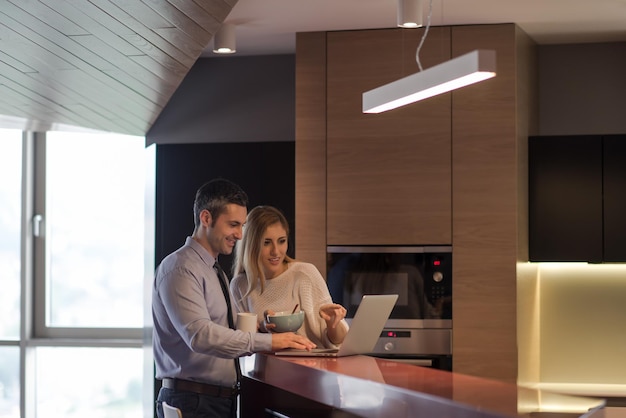 Een jong stel bereidt zich voor op de baan en gebruikt een laptop. De man drinkt koffie terwijl de vrouw samen in een luxe huis ontbijt, glimlachend naar het scherm kijkend.