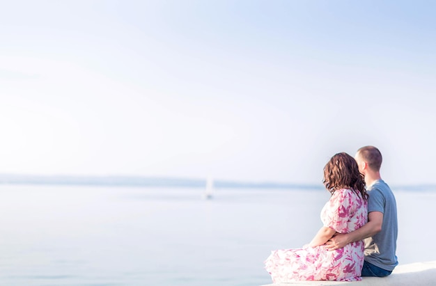 Een jong stel, een jongen en een meisje, zitten aan de oever van het meer en kijken in de verte Verliefde paar Valentijnsdag