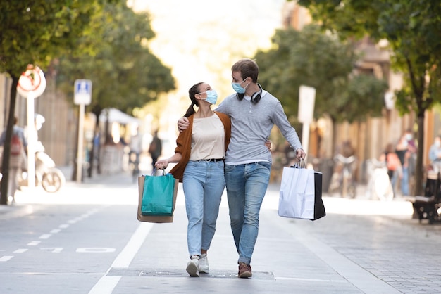 Een jong stel loopt door een voetgangersstraat met weinig boodschappentassen met medische gezichtsmaskers