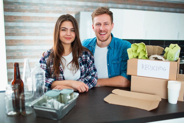 Een jong stel sorteert afval in de keuken. De jonge man en de vrouw sorteren recycleerbare voorwerpen in de keuken. Er is karton, papier, ijzer, plastic en glas en andere materialen die gerecycled kunnen worden.