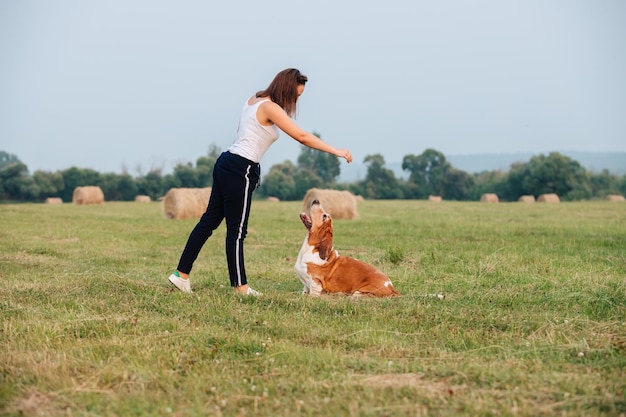 Een jong volwassen meisje loopt met een Basset Hound-hond in de natuur. De eigenaar speelt met het huisdier.
