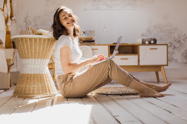 Een jonge aantrekkelijke vrouw in een licht, modern appartement gebruikt een laptop om te communiceren of online foto's van hoge kwaliteit te bestuderen