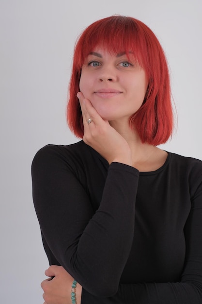 Een jonge aantrekkelijke vrouw met een kort oranje kapsel in een zwart T-shirt en spijkerbroek poserend in de studio op een witte achtergrond