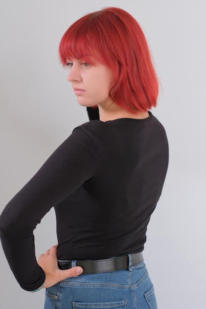 Een jonge aantrekkelijke vrouw met een kort oranje kapsel in een zwart T-shirt en spijkerbroek poserend in de studio op een witte achtergrond