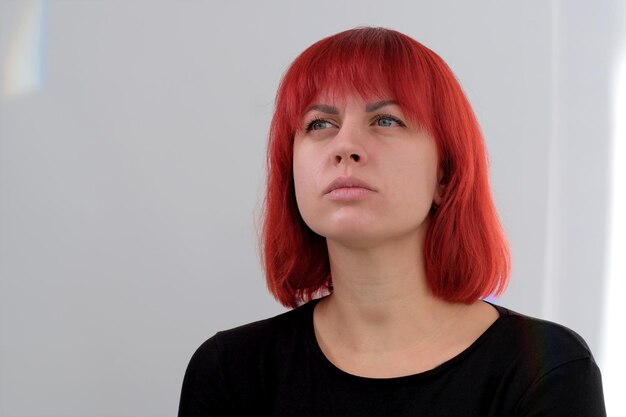 Een jonge aantrekkelijke vrouw met een kort oranje kapsel in een zwart T-shirt en spijkerbroek poserend in de studio op een witte achtergrond