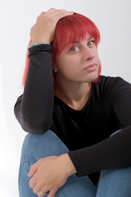 Een jonge aantrekkelijke vrouw met een kort oranje kapsel in een zwart T-shirt en spijkerbroek poserend in de studio op een witte achtergrond