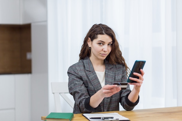 Een jonge aantrekkelijke vrouw voert haar creditcardgegevens in via een app op haar telefoon, die online winkelt