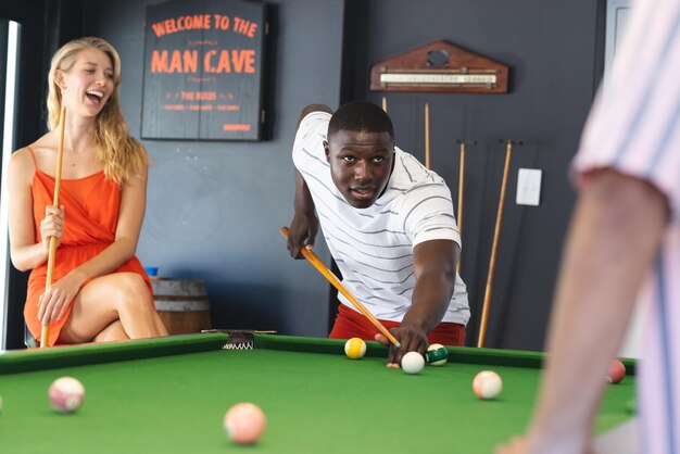 Foto een jonge afro-amerikaanse man richt zich op een pool shot terwijl een jonge blanke vrouw lacht