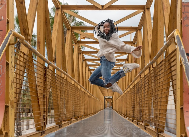 Een jonge Afro-Amerikaanse vrouw met vlechten die op een gele brug springt