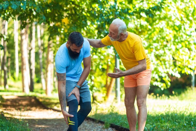 Een jonge atleet heeft een beenblessure terwijl een oudere atleet hem helpt