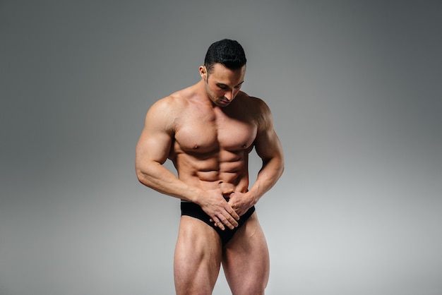 Een jonge atleetbodybuilder poseert topless in de studio en pronkt met zijn buikspieren en spieren