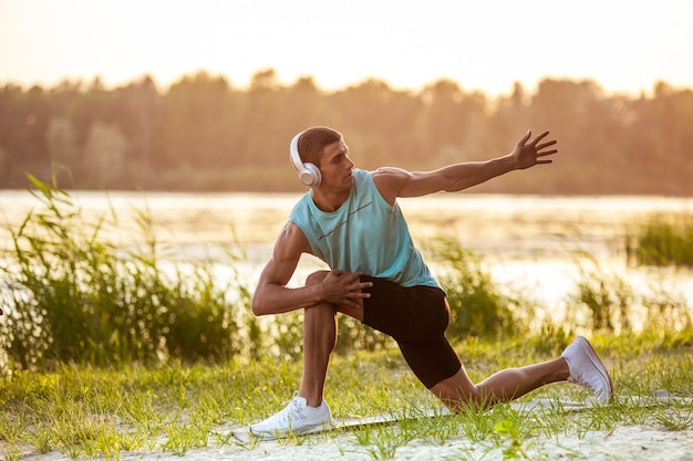 Een jonge atletische man die aan het trainen is en buiten aan de rivier naar de muziek luistert