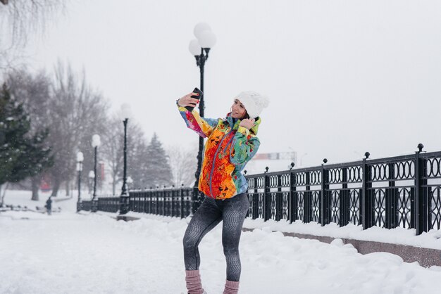 Een jonge atletische vrouw maakt een selfie op een ijzige en besneeuwde dag. fitness, recreatie