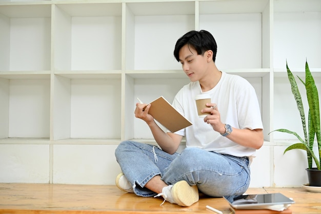 Een jonge Aziatische man die koffie drinkt tijdens het lezen van een boek Hobby- en vrijetijdsconcept