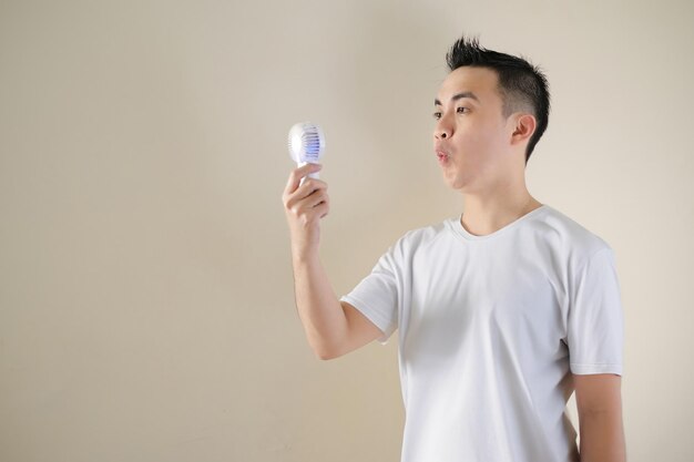 Foto een jonge aziatische man voelt zich opgelucht bij het gebruik van een draagbare ventilator vanwege het hete weer