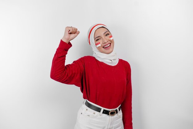 Een jonge Aziatische moslimvrouw met een gelukkige, succesvolle uitdrukking in een rode top en een witte hijab geïsoleerd door een witte achtergrond Indonesië's onafhankelijkheidsdag concept