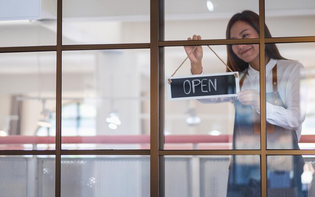 Een jonge Aziatische ondernemer of een serveerster die een open bord aan de voordeur van de winkel hangt